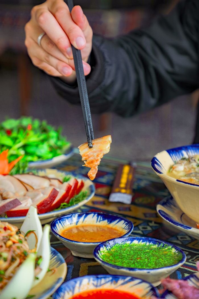 Chopsticks holding seafood over a vibrant meal with various dishes and sauces.